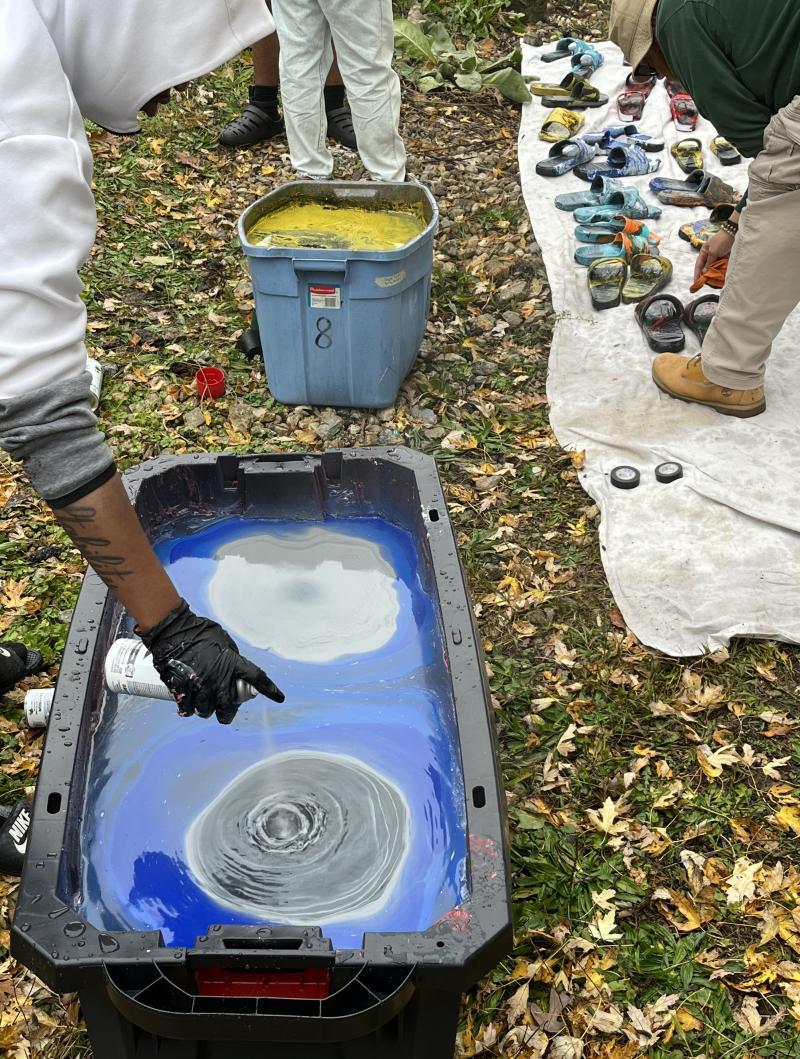 Student spraying spray various colors of paint on top of water to dunk their sandals in a "hydro-dip"